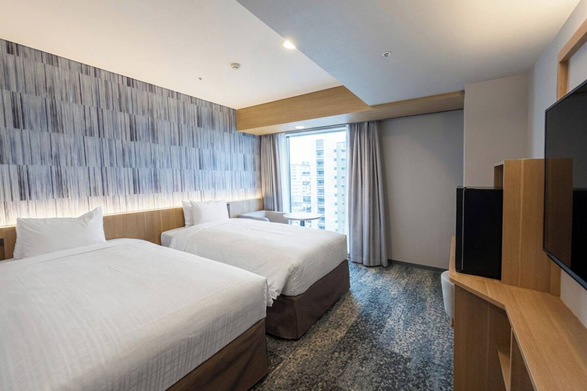Habitación de hotel con dos camas, un ventanal grande, un televisor de pantalla plana y un diseño moderno en la pared.
