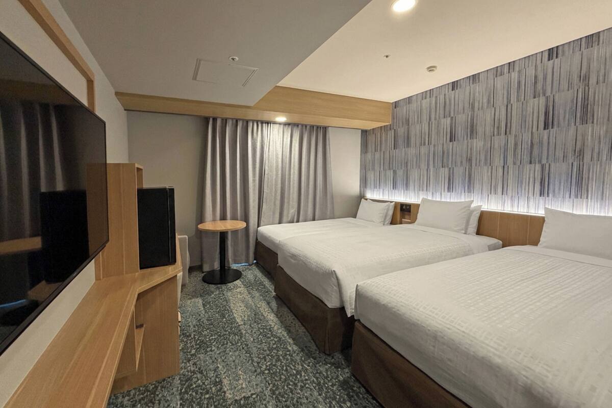 Habitación de hotel con dos camas, un televisor, una mesita y una pared con diseño texturizado.
