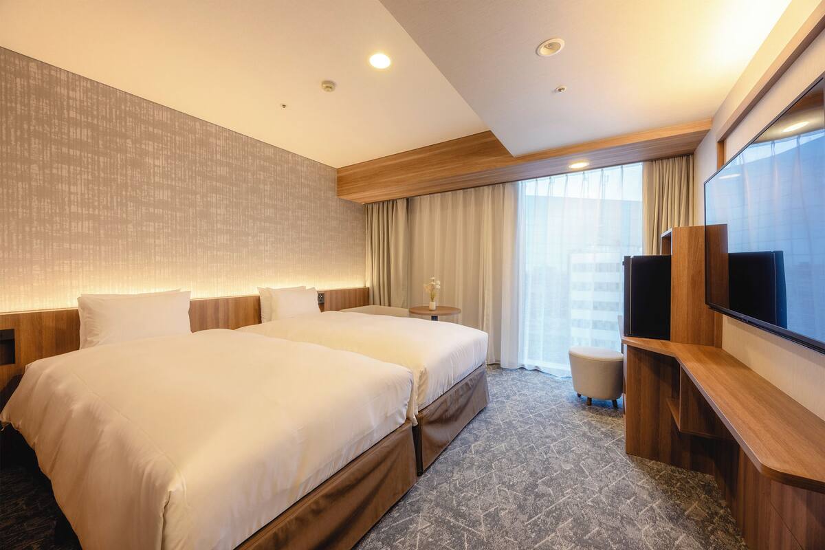 Habitación de hotel con dos camas, un televisor y una mesita con un jarrón.