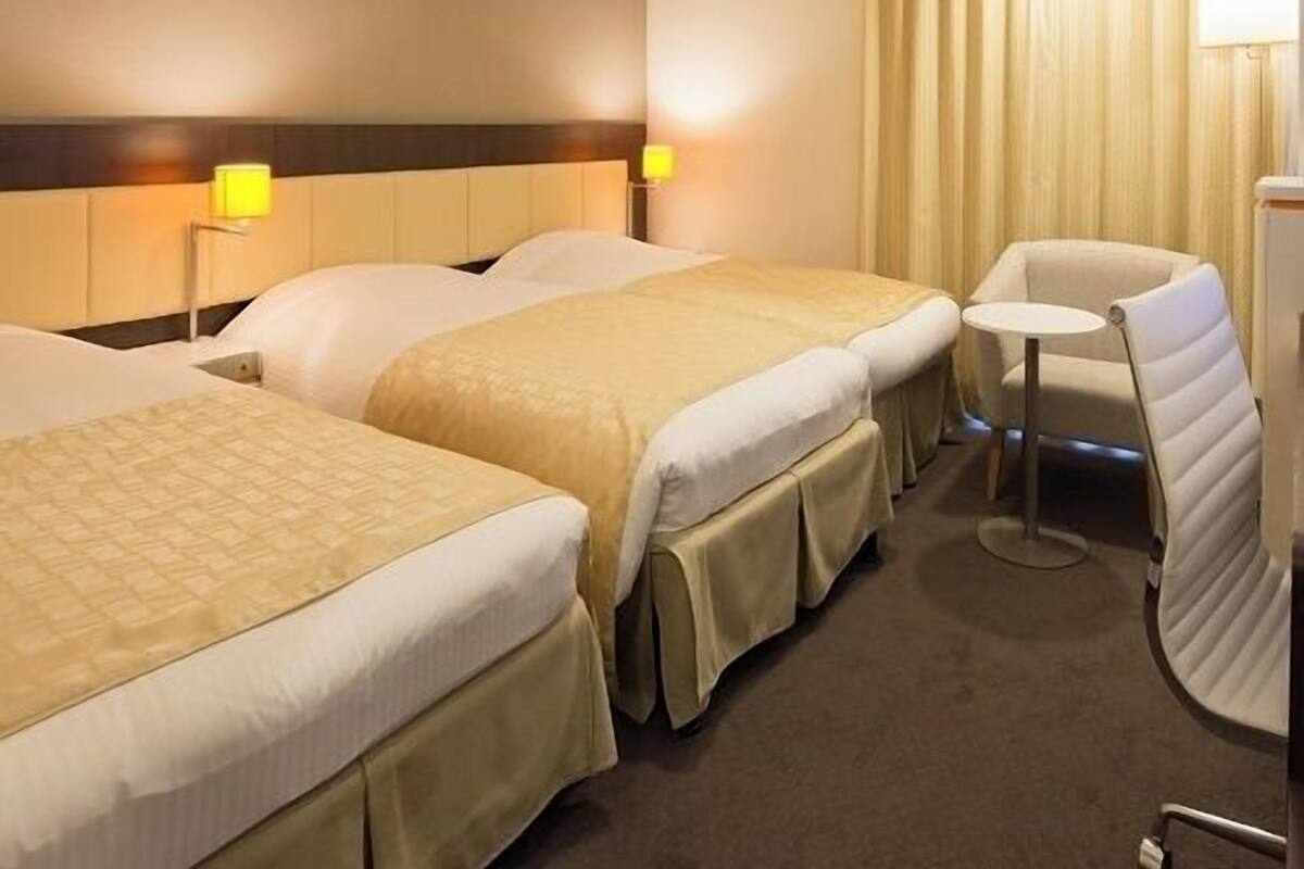 Habitación de hotel con dos camas, una mesita redonda pequeña y una silla.