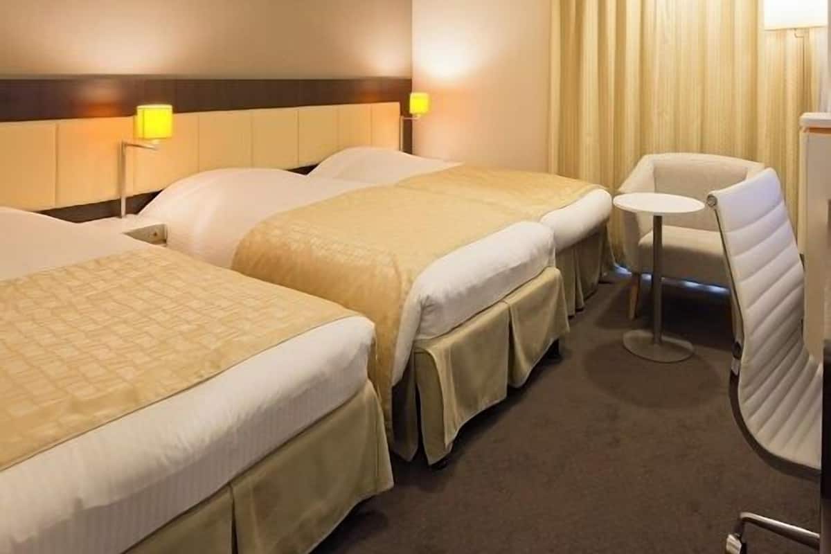 Habitación de hotel con dos camas, una mesita redonda pequeña y una silla.