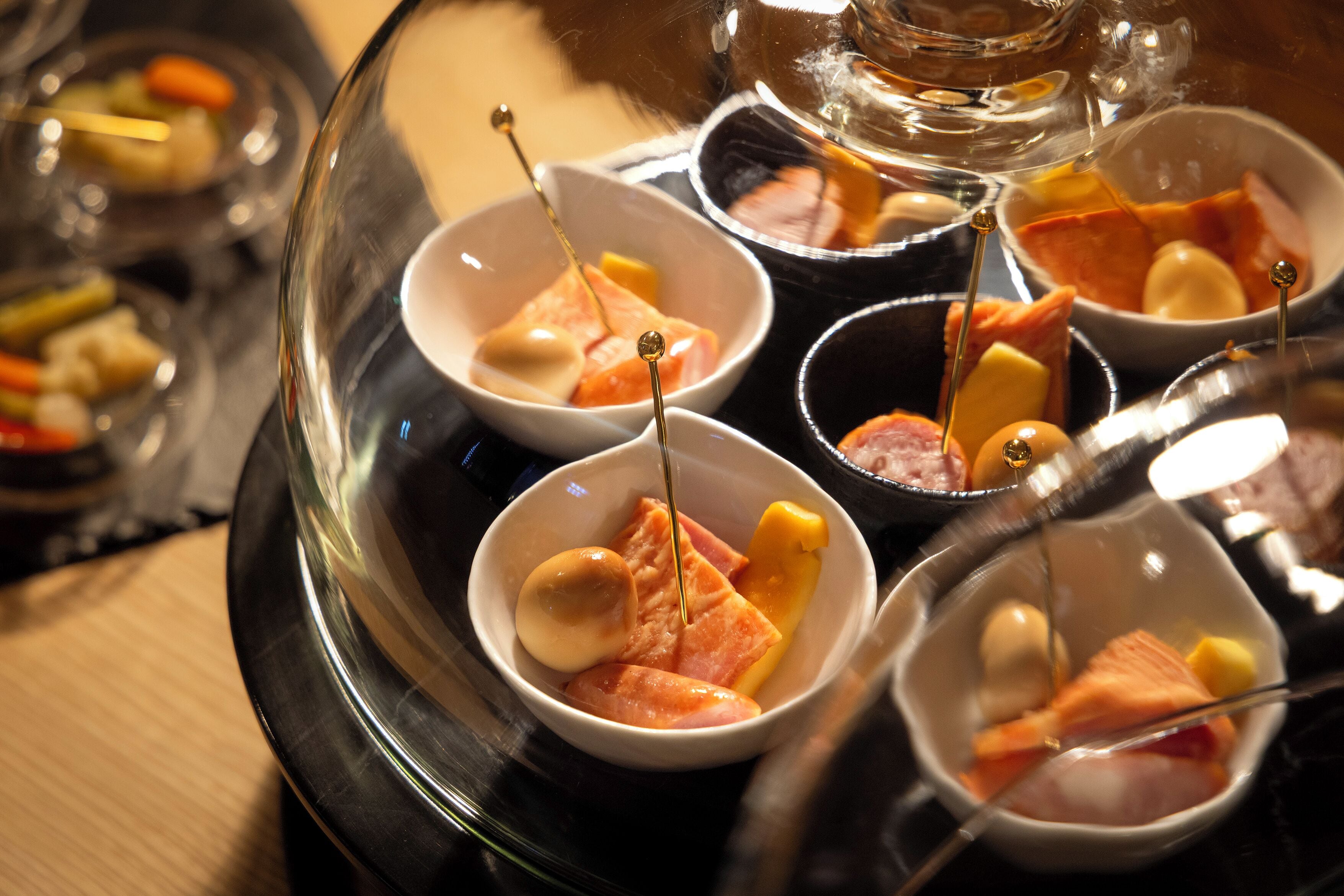A glass dome over a tray of food items, including various meats and vegetables.