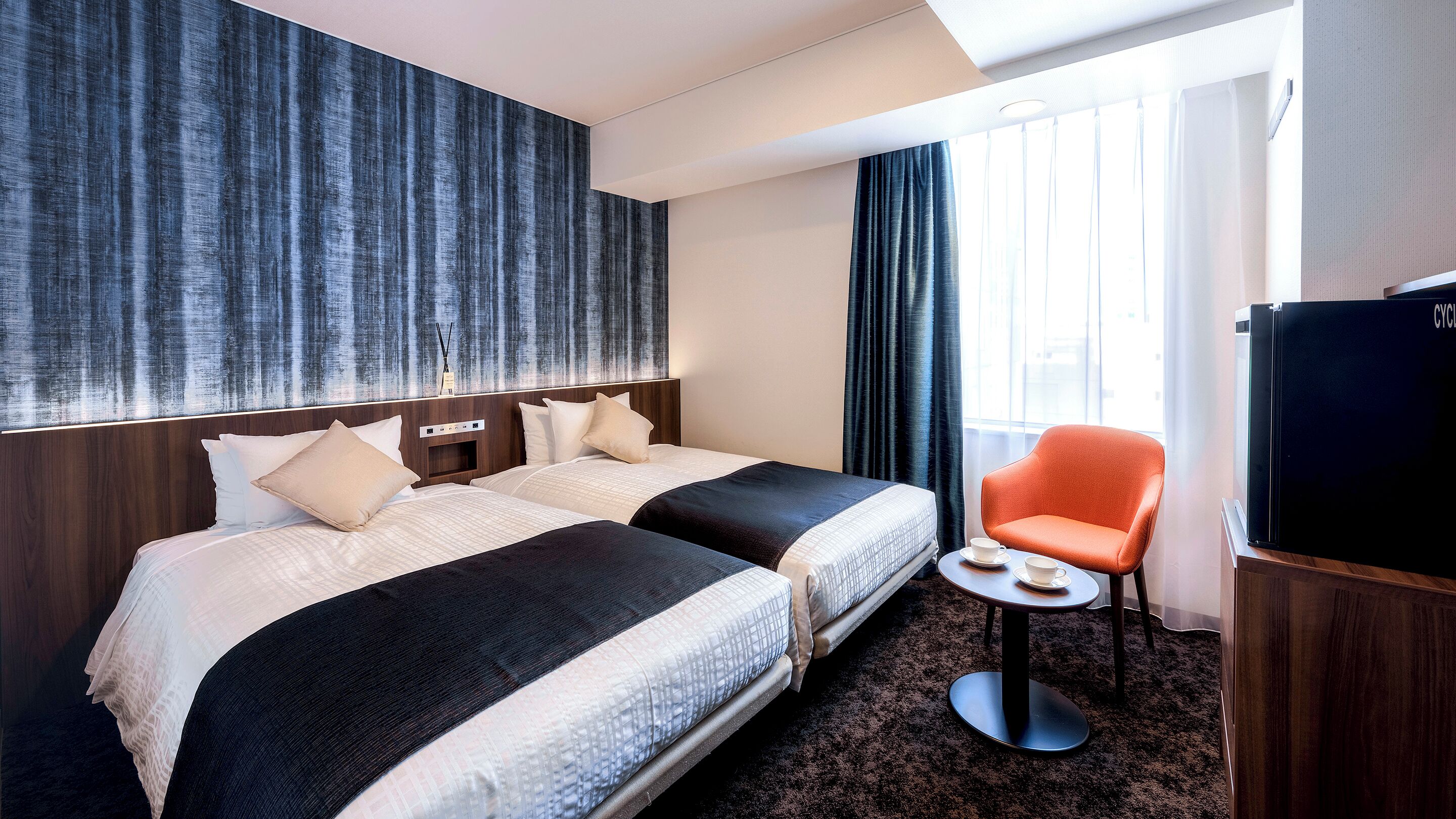 Habitación de hotel con dos camas, una mesita con tazas, una silla y un televisor.