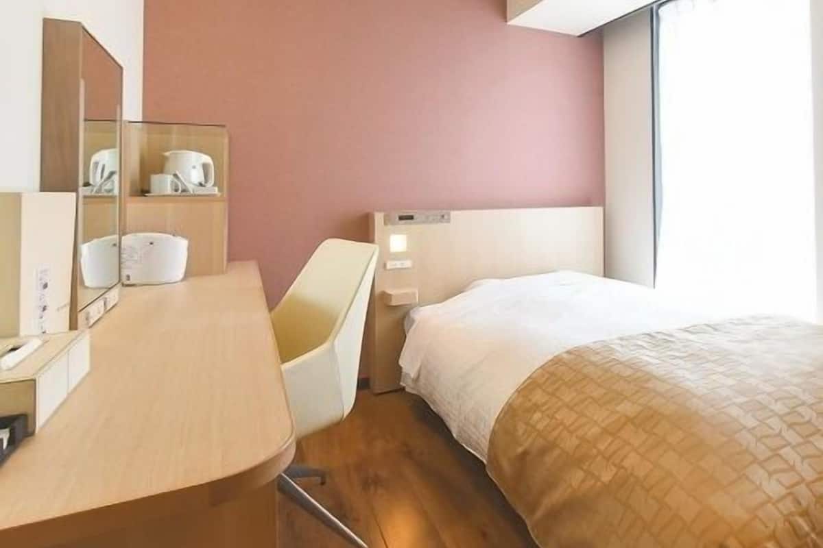 Una habitación de hotel con cama, escritorio, silla, espejo y ventana.