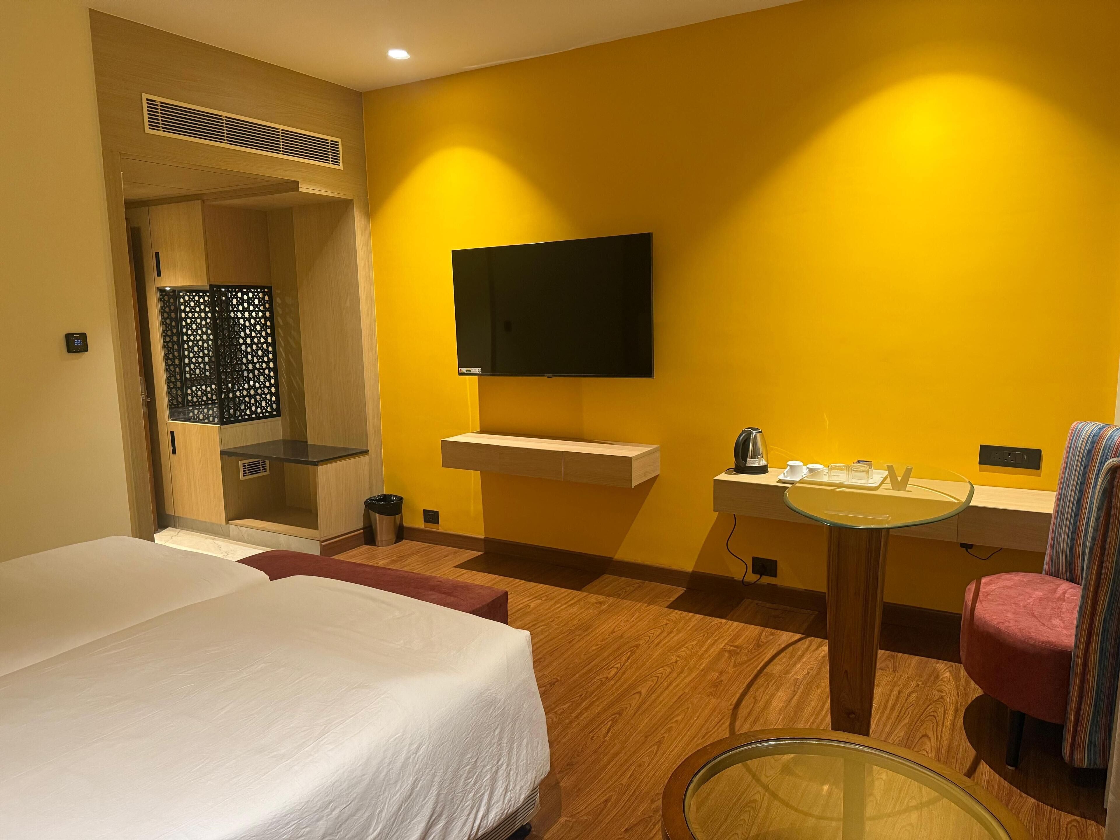 Une chambre d’hôtel avec un lit, une petite table avec une bouilloire, une chaise et un téléviseur fixé au mur.
