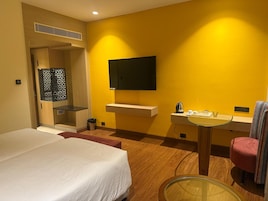 Una habitación de hotel con una cama, una mesita con hervidor, una silla y un televisor en la pared.