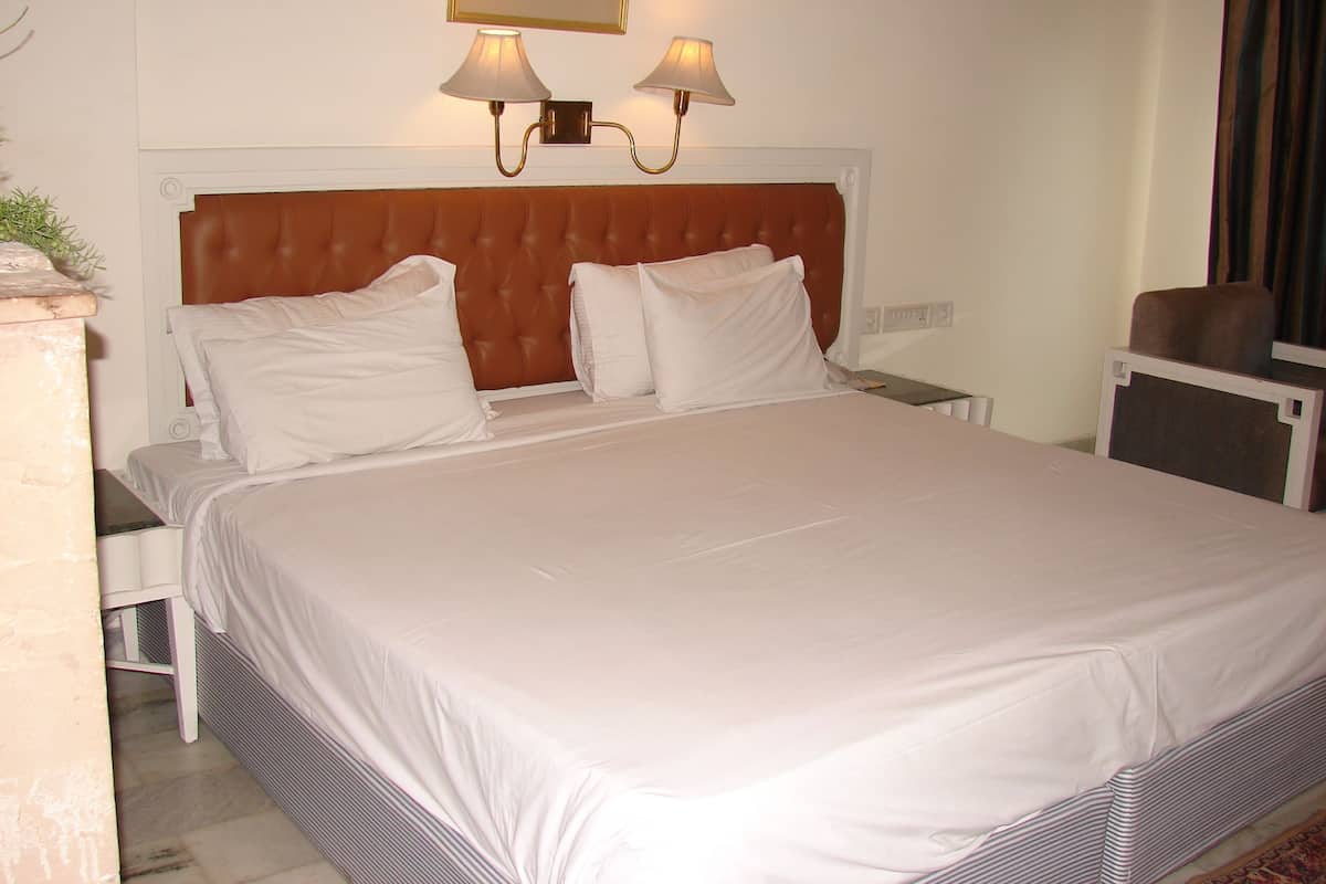 Una cama bien hecha con sábanas blancas, un cabecero capitonado y dos lámparas fijadas a la pared.