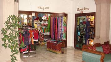 Un elegante vestíbulo de hotel boutique con una zona de estar, una planta y dos tiendas llamadas 'KHAZANA' y 'GEMS N ARTS'.