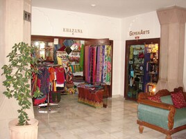 Un elegante vestíbulo de hotel boutique con una zona de estar, una planta y dos tiendas llamadas 'KHAZANA' y 'GEMS N ARTS'.