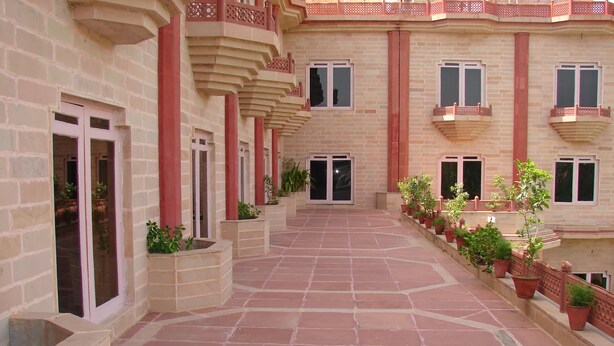 Un patio con suelo de baldosas, plantas en macetas y un edificio con múltiples ventanas y balcones.