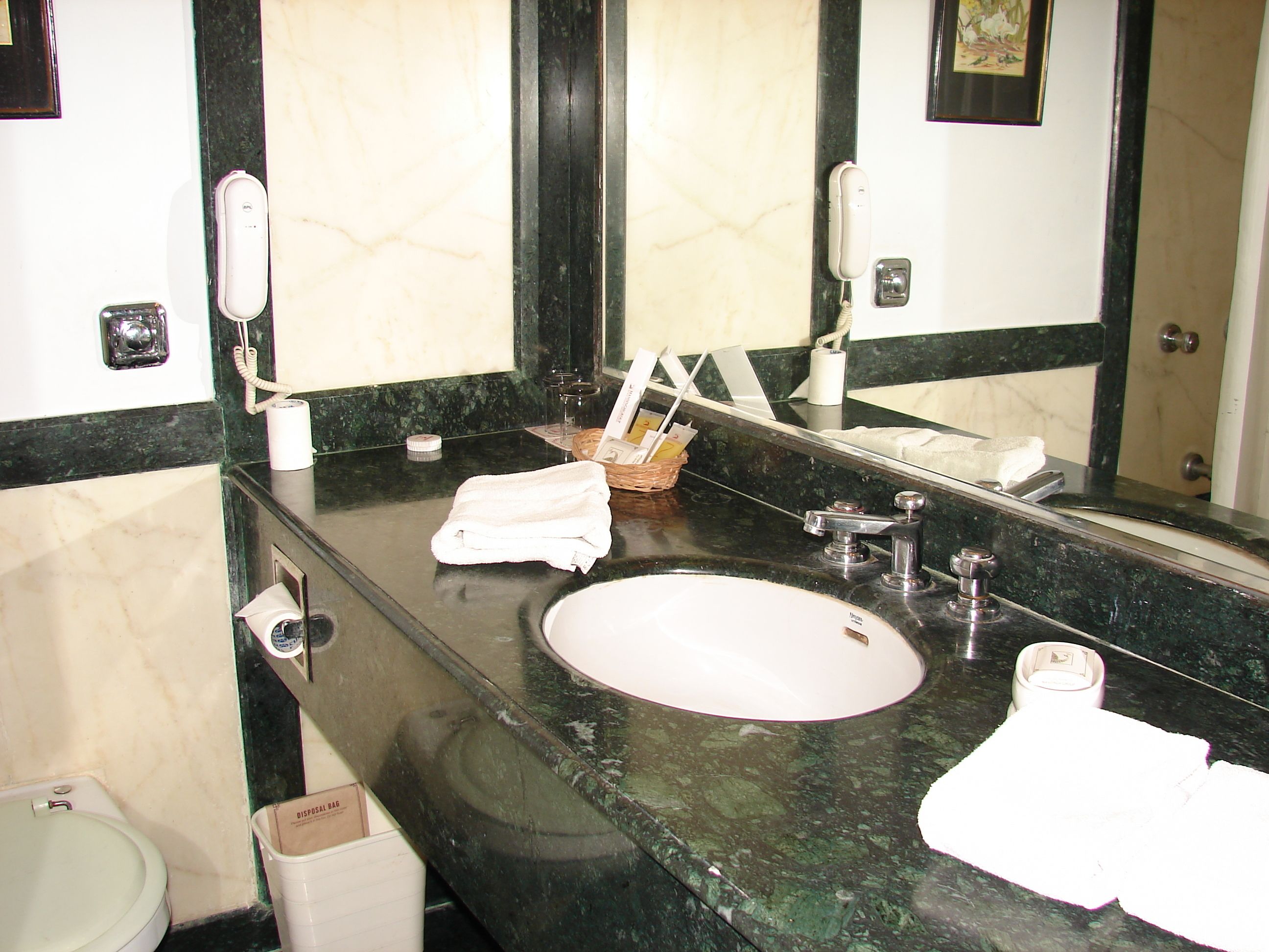 A bathroom with a marble sink, a mirror, a towel, and a trash bin.