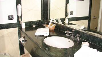 A bathroom with a marble sink, a mirror, a towel, and a trash bin.