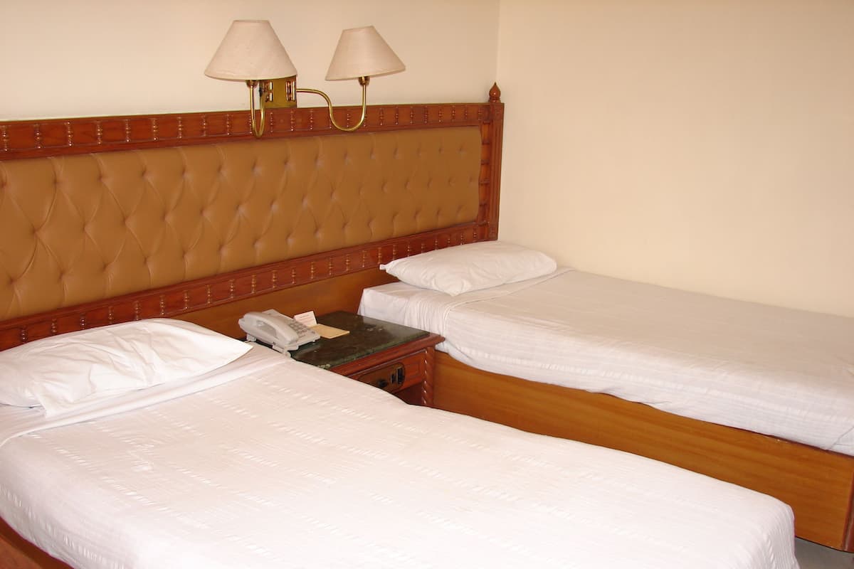 Habitación de hotel con dos camas individuales, cabecero de madera, mesita de noche con teléfono y dos lámparas de pared.