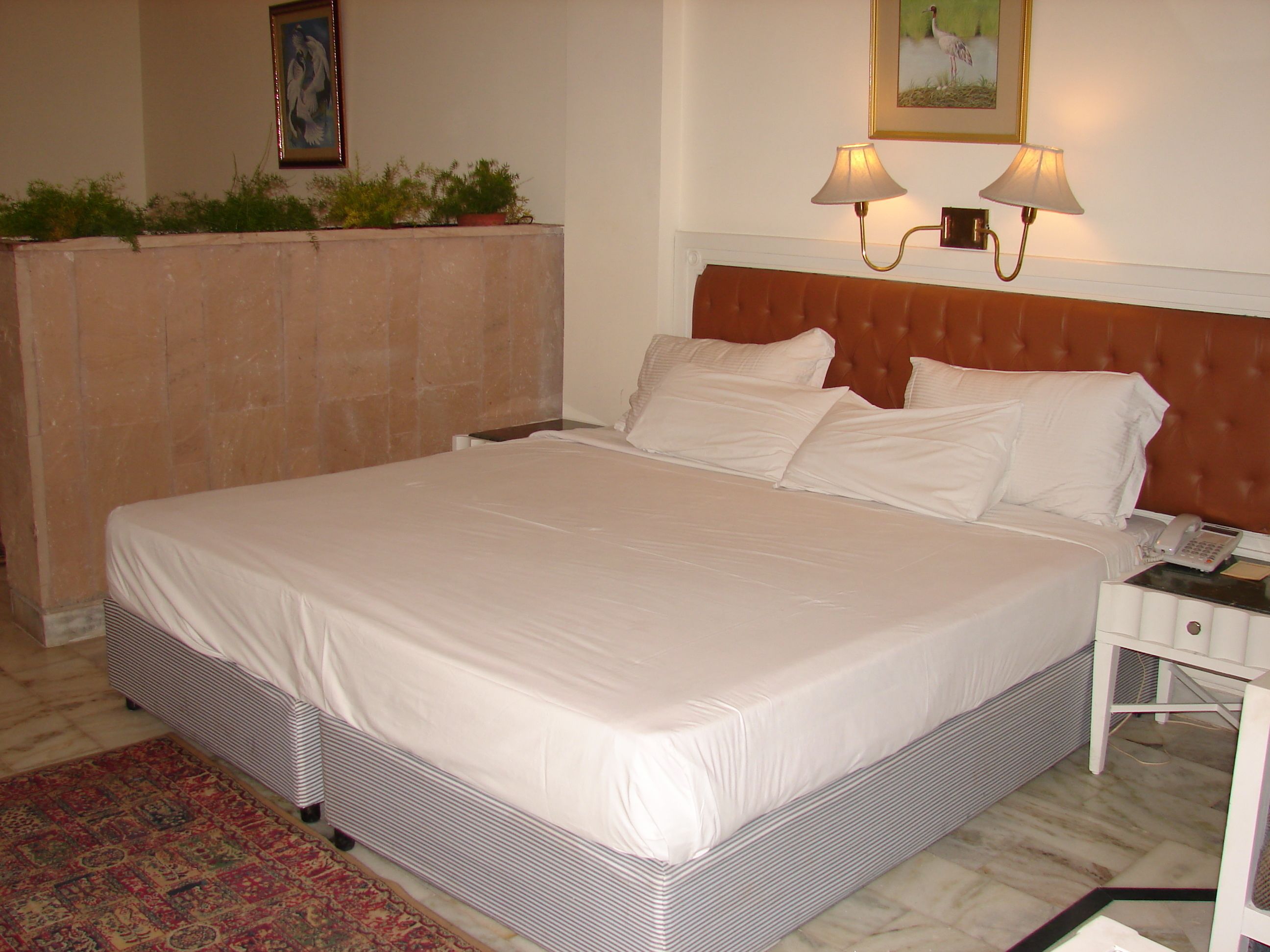 A neatly made bed with white linens, a brown headboard, and a bedside table with a lamp and a telephone.
