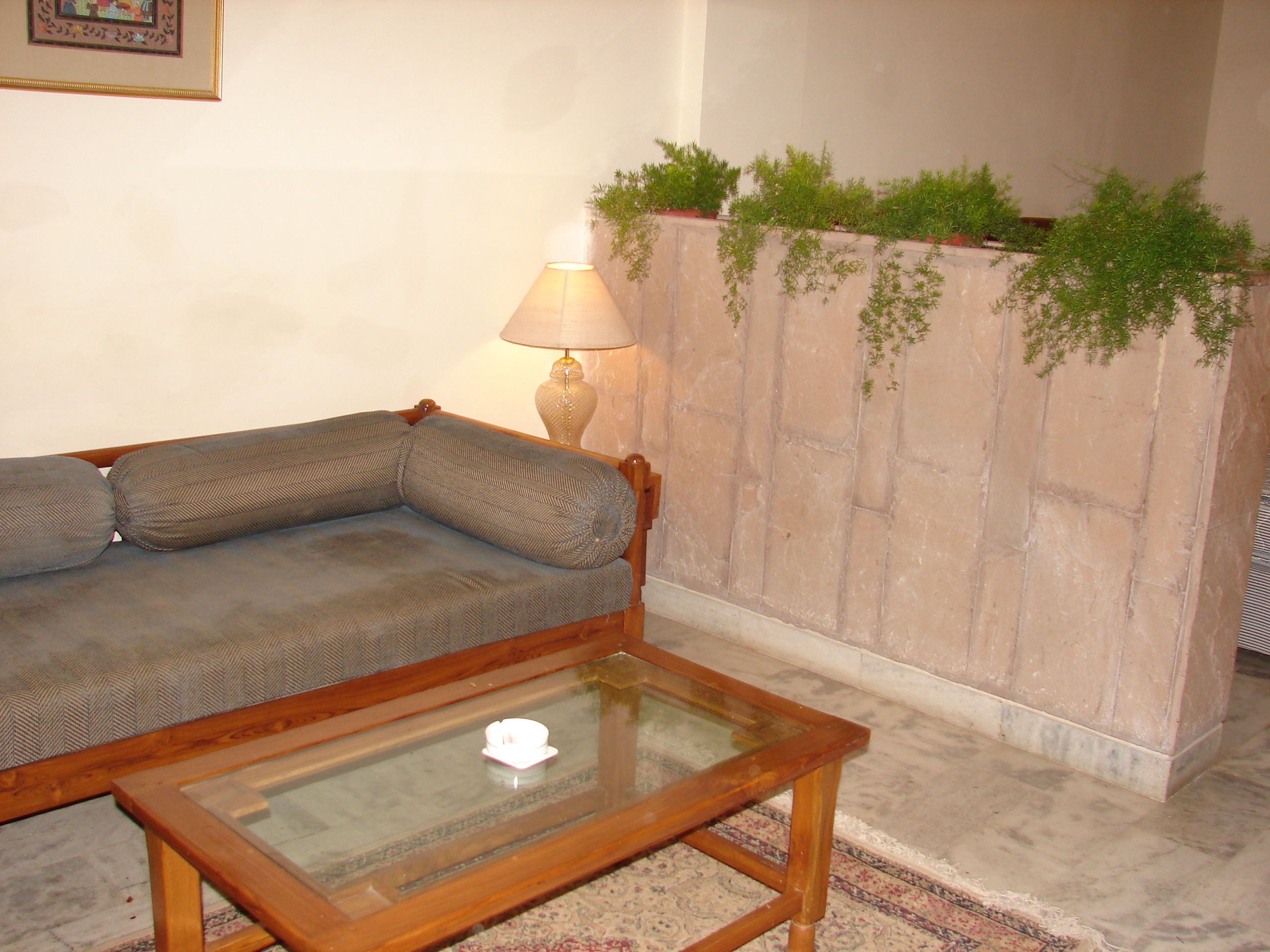 A living room with a sofa, a glass-top coffee table, a lamp, and a stone wall with plants.