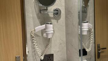 Un baño con pared de mármol, un espejo redondo, un secador de pelo, un lavabo con encimera negra y un armario para espejo.