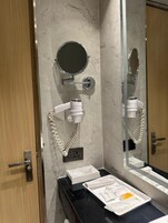 Un baño con pared de mármol, un espejo redondo, un secador de pelo, un lavabo con encimera negra y un armario para espejo.