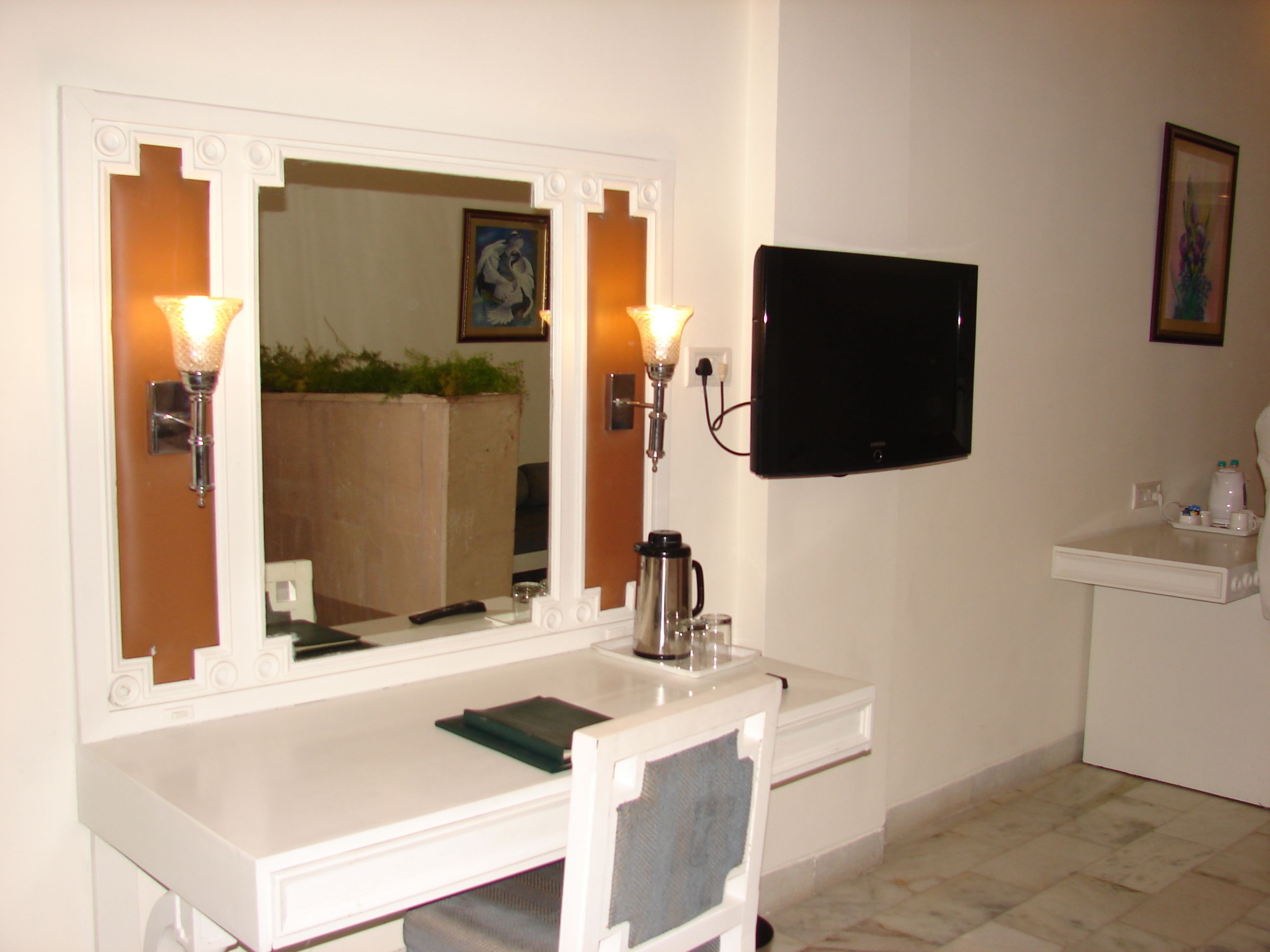 A bathroom with a white vanity, a large mirror with wall sconces, a black flat-screen TV mounted above the vanity, and a small sink with a mirror.