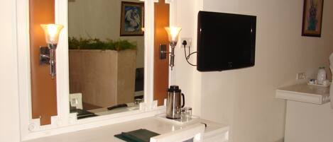 A bathroom with a white vanity, a large mirror with wall sconces, a black flat-screen TV mounted above the vanity, and a small sink with a mirror.