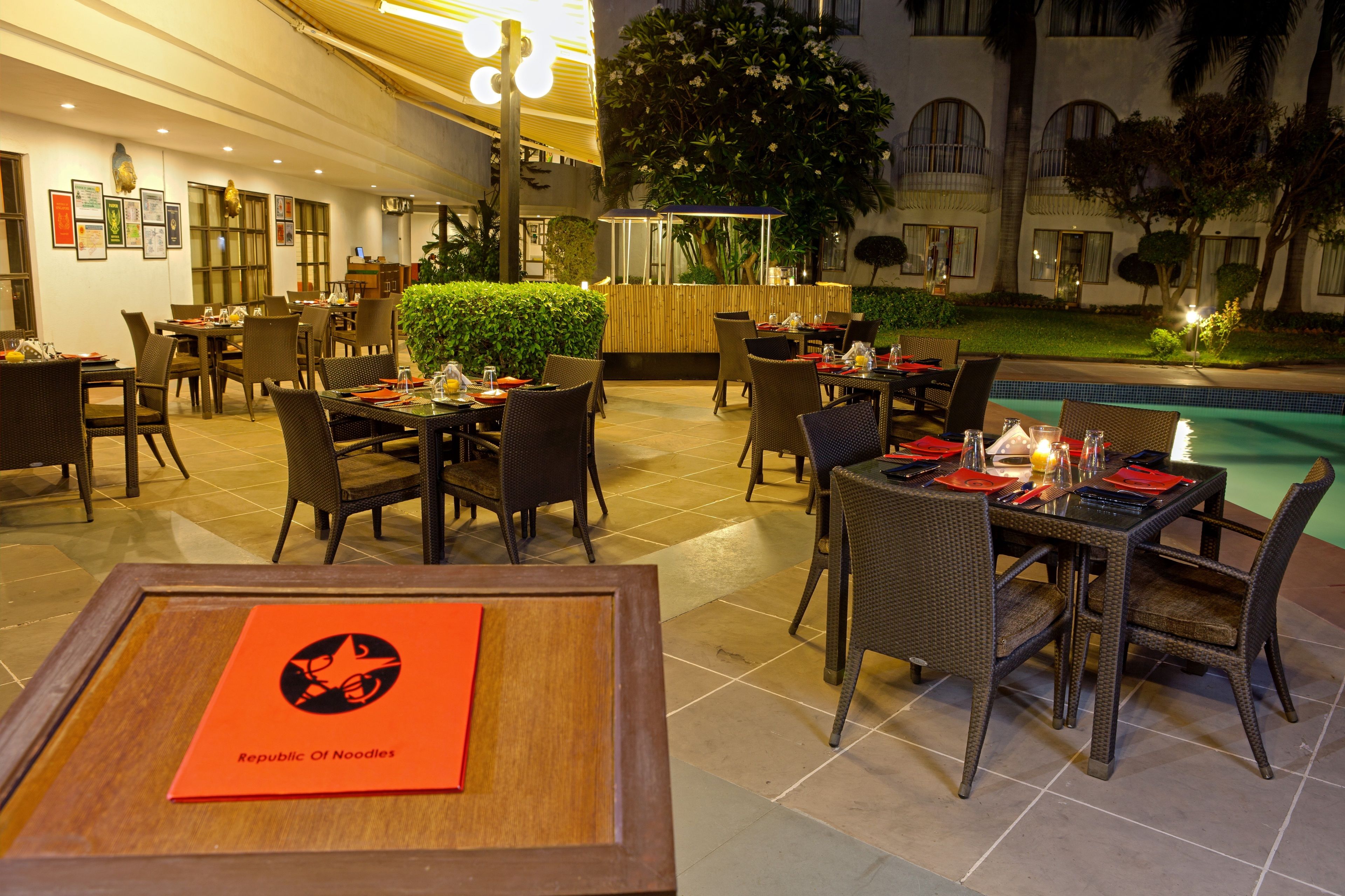 An outdoor dining area with tables and chairs, a pool, and a building in the background.