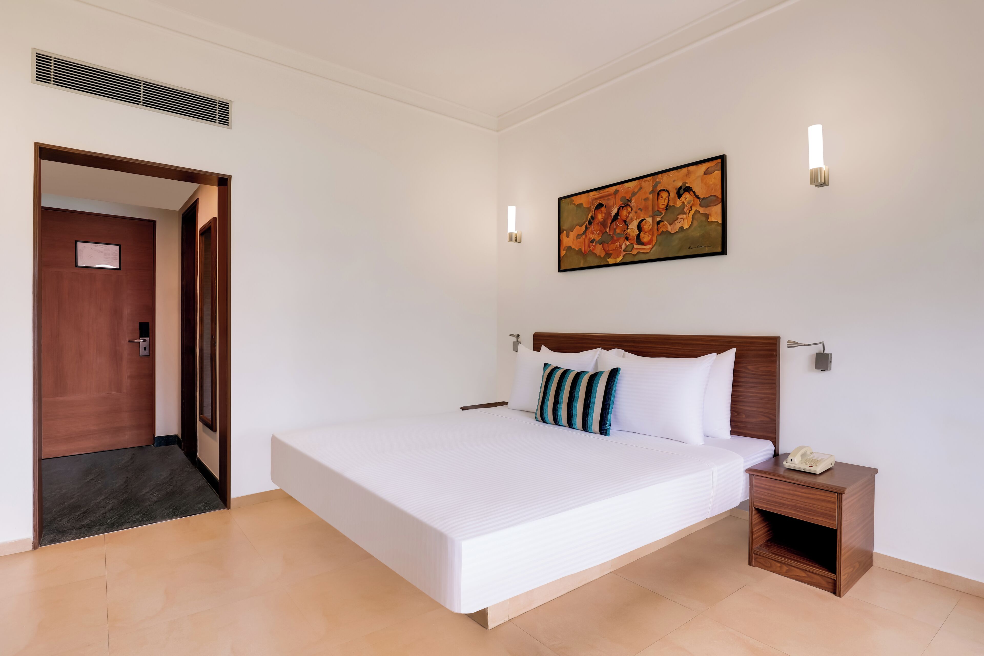 Habitación de hotel con una cama grande, cabecera de madera, mesita de noche con teléfono y un cuadro en la pared.