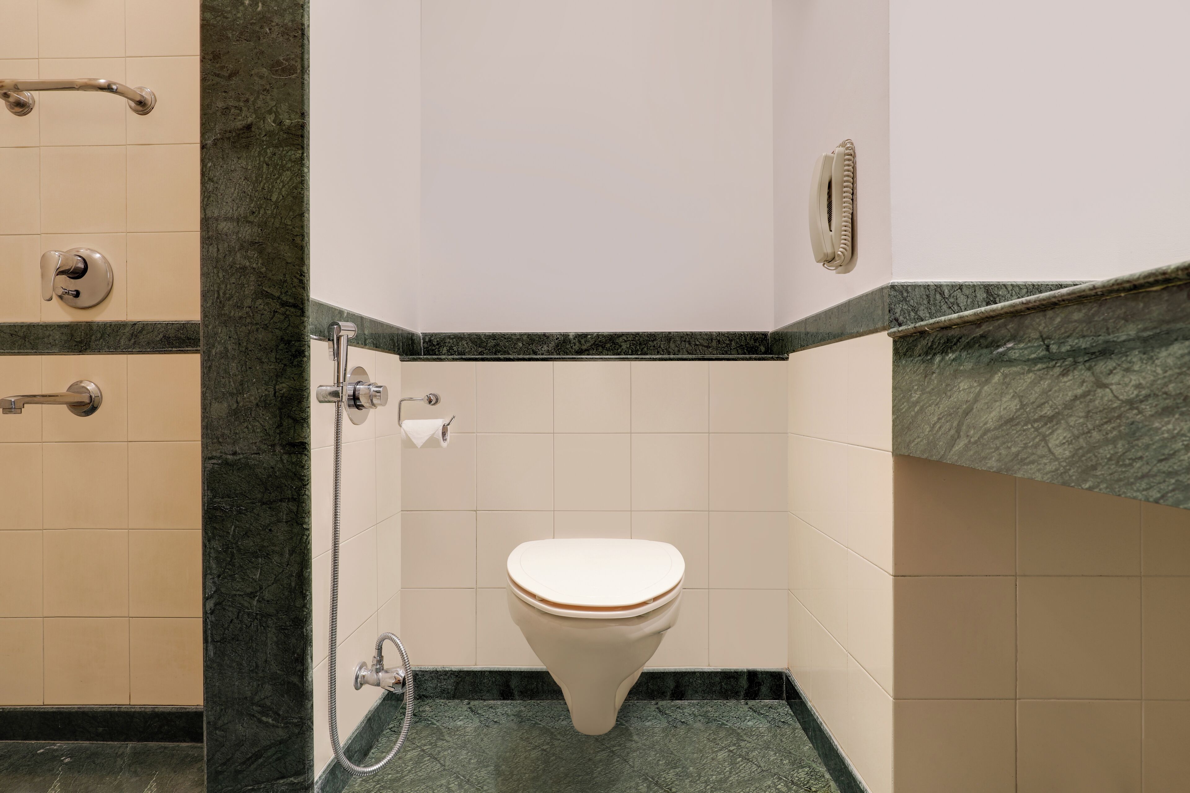 A bathroom with a toilet, grab bars, and a marble countertop.