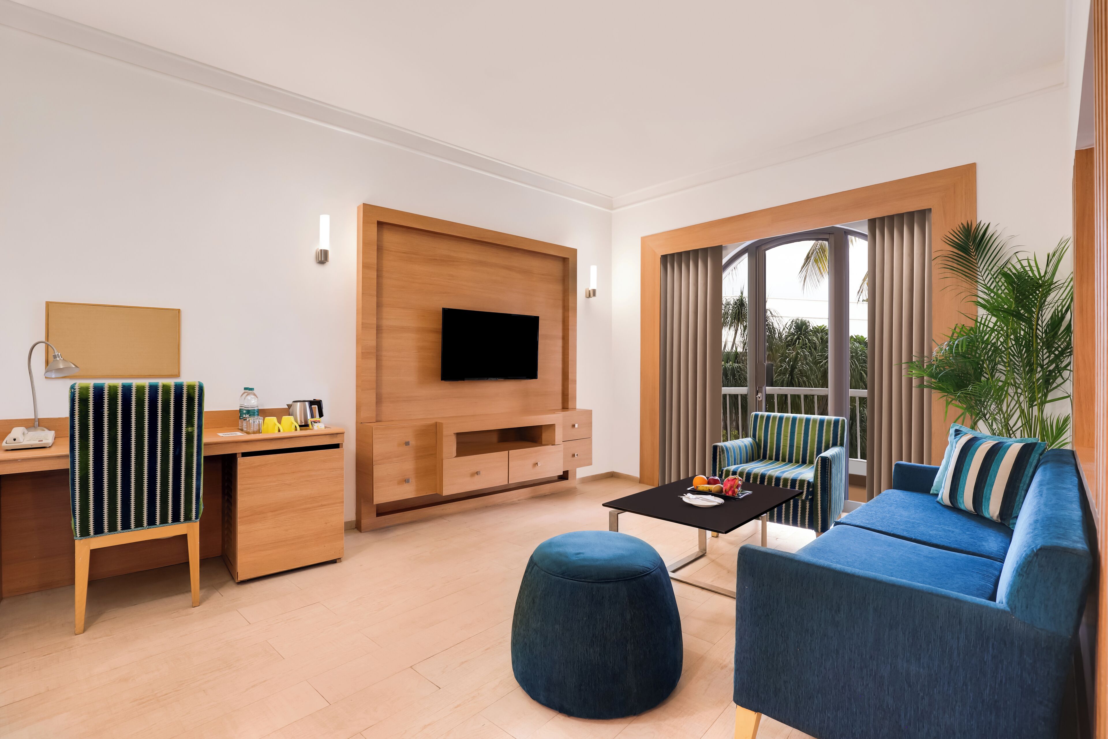 Een moderne woonkamer met een televisie, houten meubels, een bank, een poef en een eettafel.