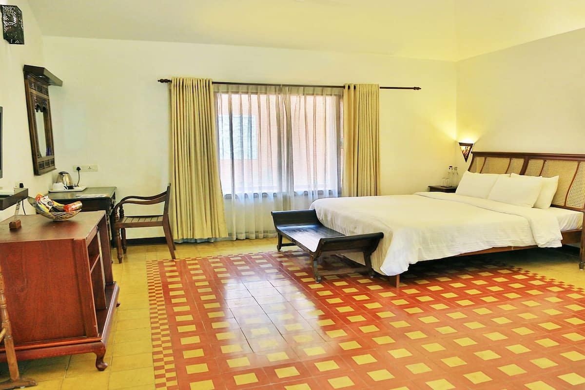Quarto de hotel com cama, escrivaninha, televisão e janela com cortinas.
