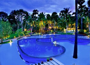 A resort pool area with multiple circular pools, palm trees, and lounge chairs.