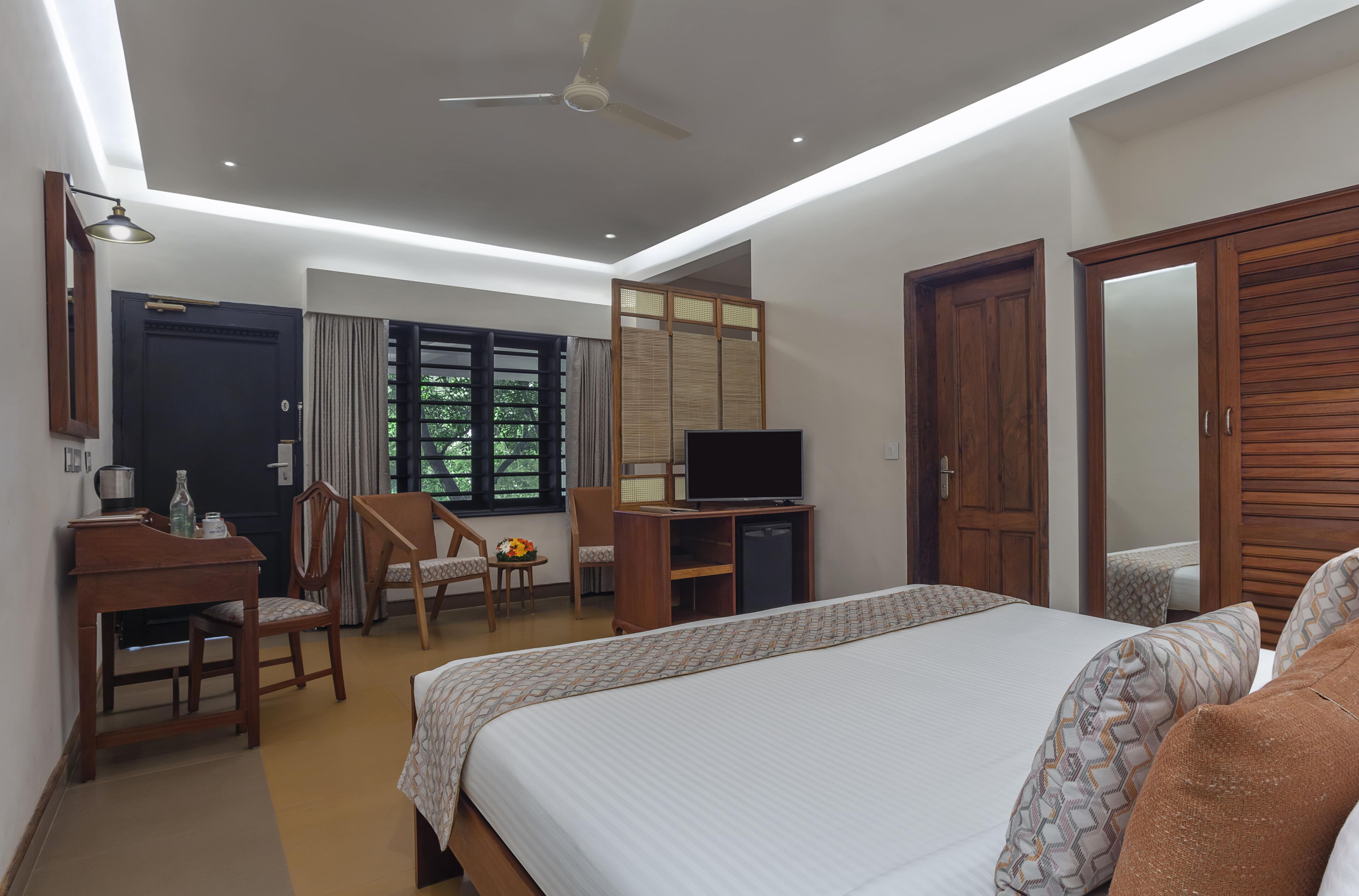 A hotel room with a bed, desk, chair, TV, wardrobe, and a window with curtains.
