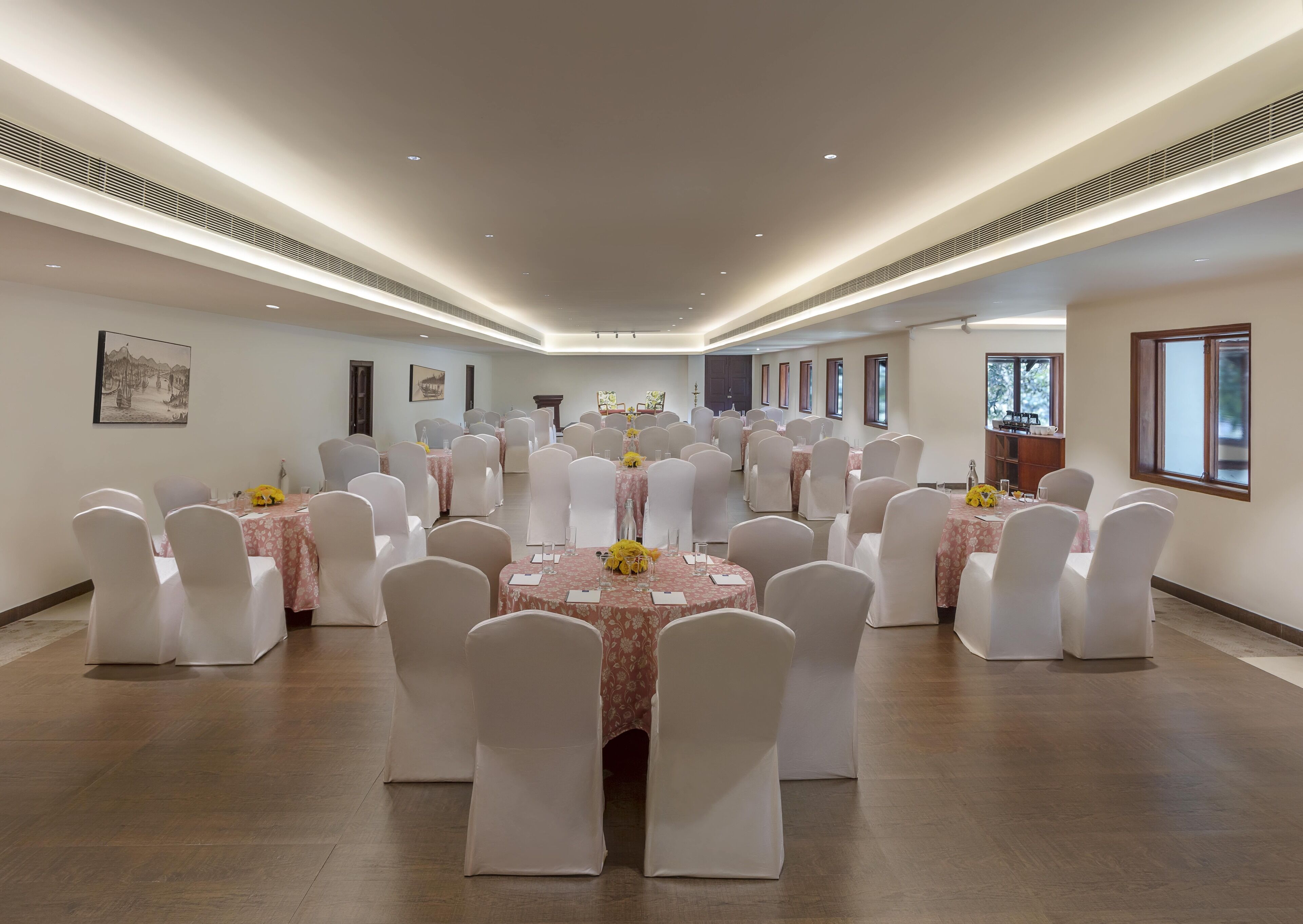 Un salón de banquetes con mesas redondas, sillas blancas y centros de mesa florales.