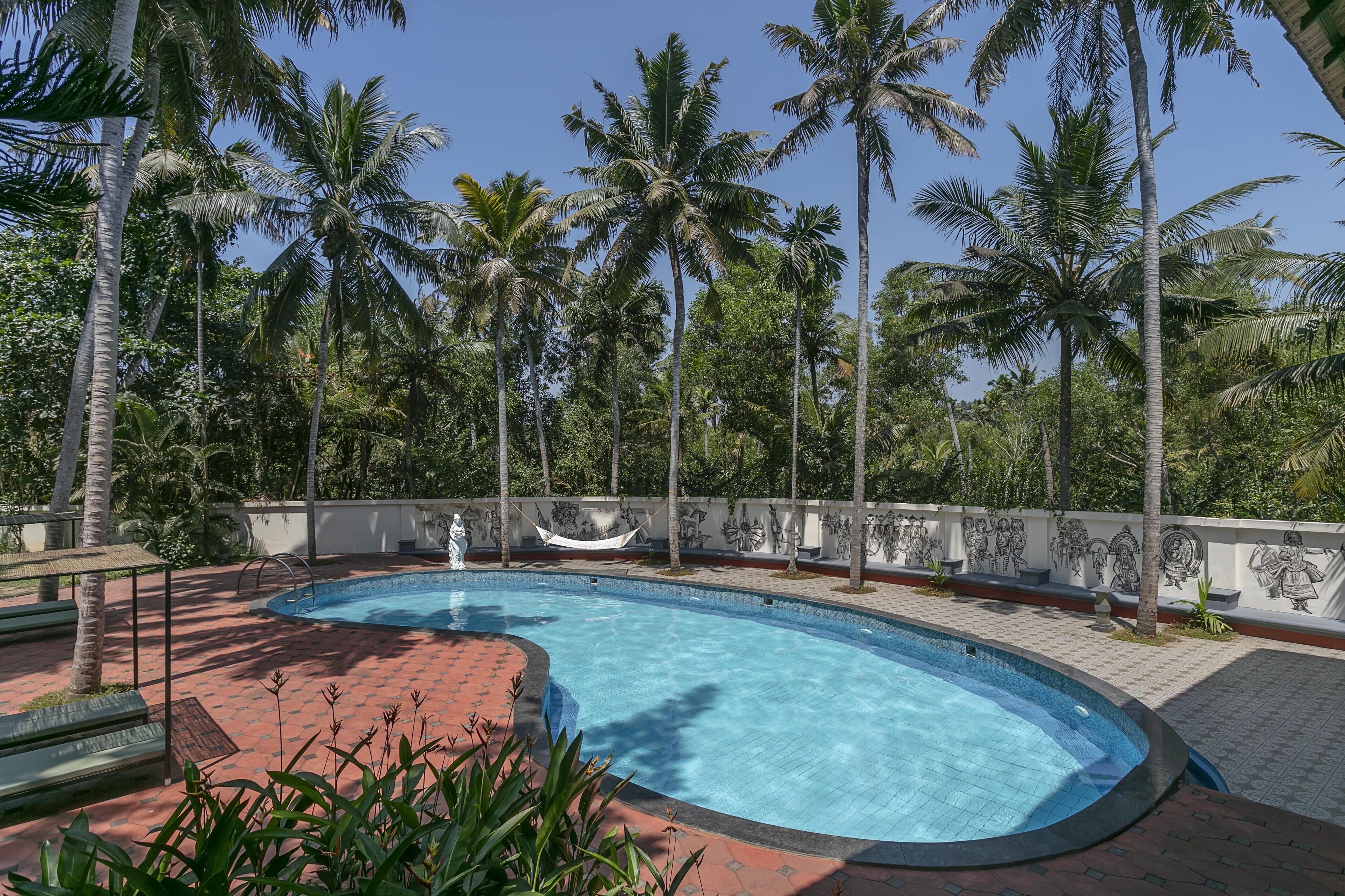 Ein Swimmingpool, umgeben von Palmen und einer Wand mit Wandmalerei.