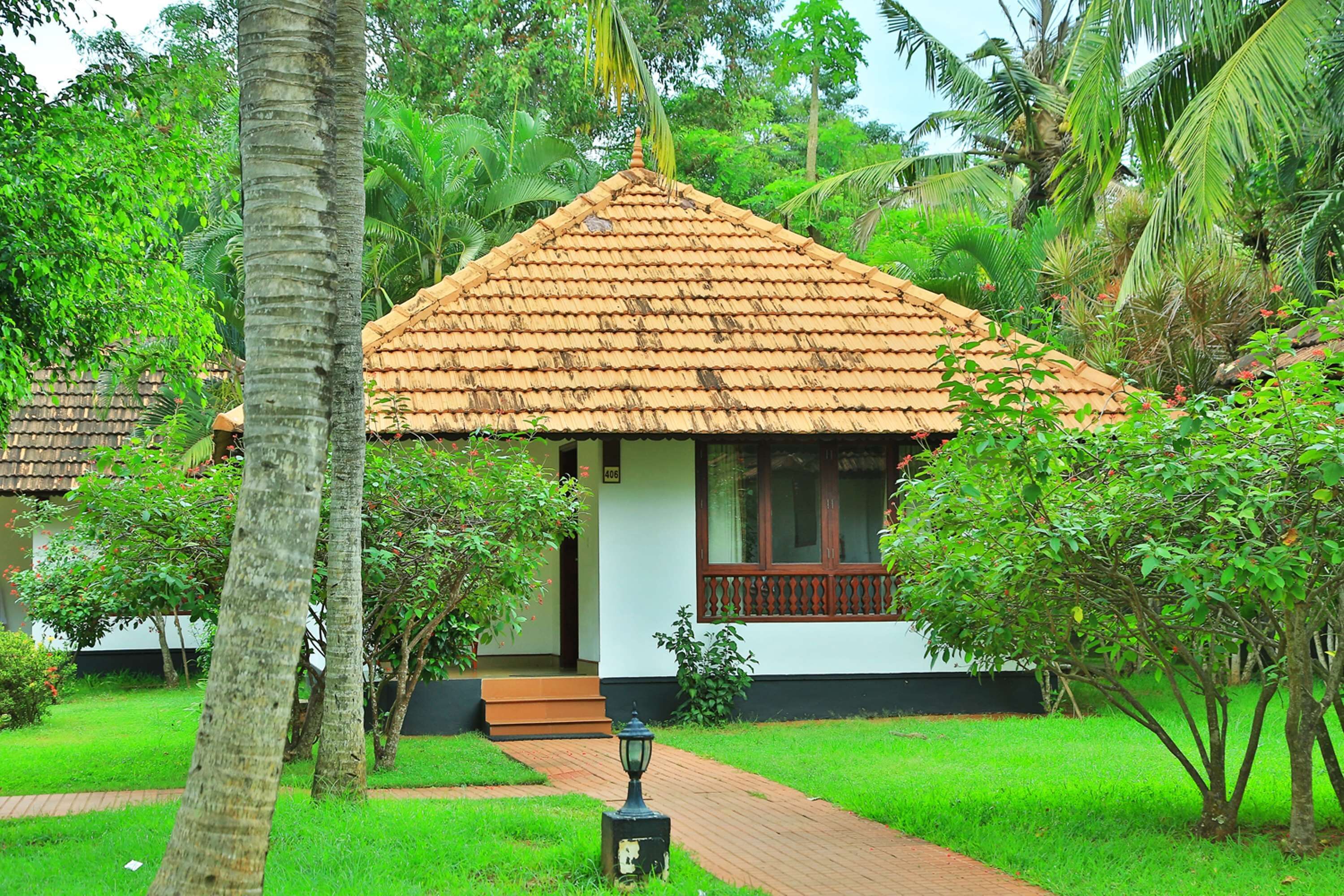 A bungalow with a tiled roof, surrounded by lush greenery and palm trees.