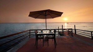 Une table avec un parasol et des chaises sur une terrasse au bord de l’eau, au coucher du soleil.