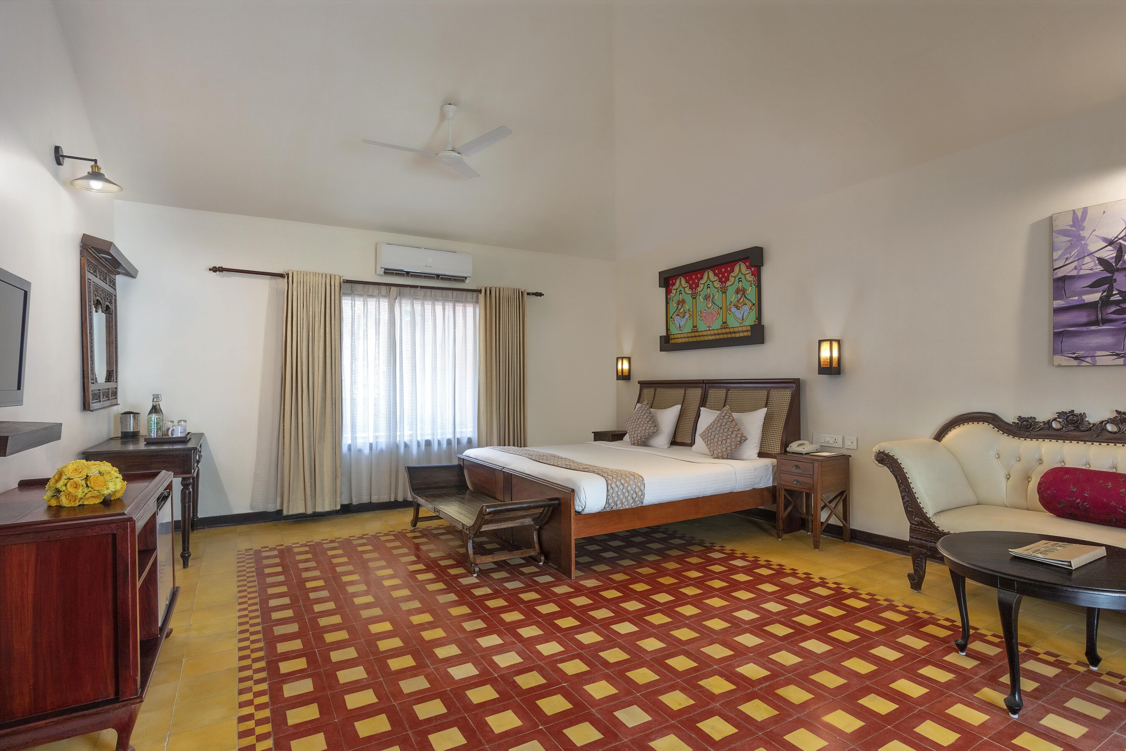 Ein Hotelzimmer mit Bett, Sofa, Schreibtisch, Stuhl, Fernseher und Deckenventilator.