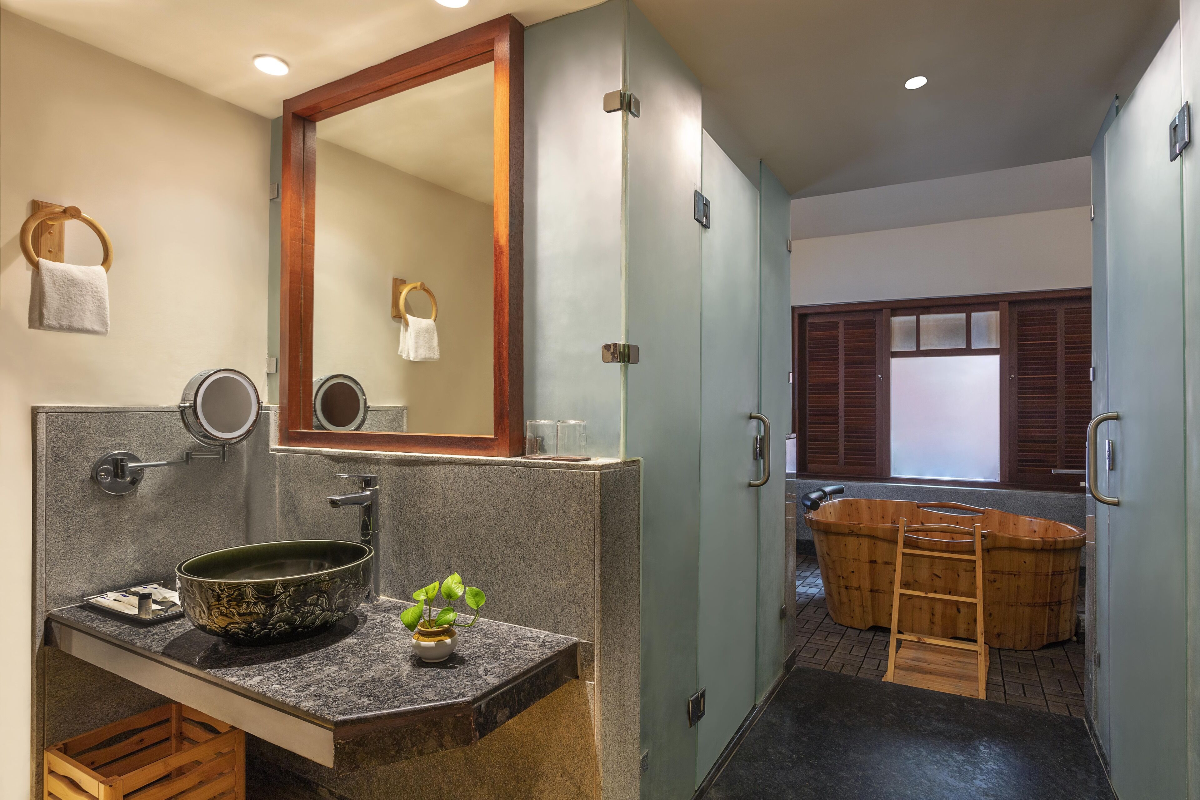 A bathroom with a large mirror, a sink with a bowl, a towel rack, and a wooden ladder leading to a bathtub.