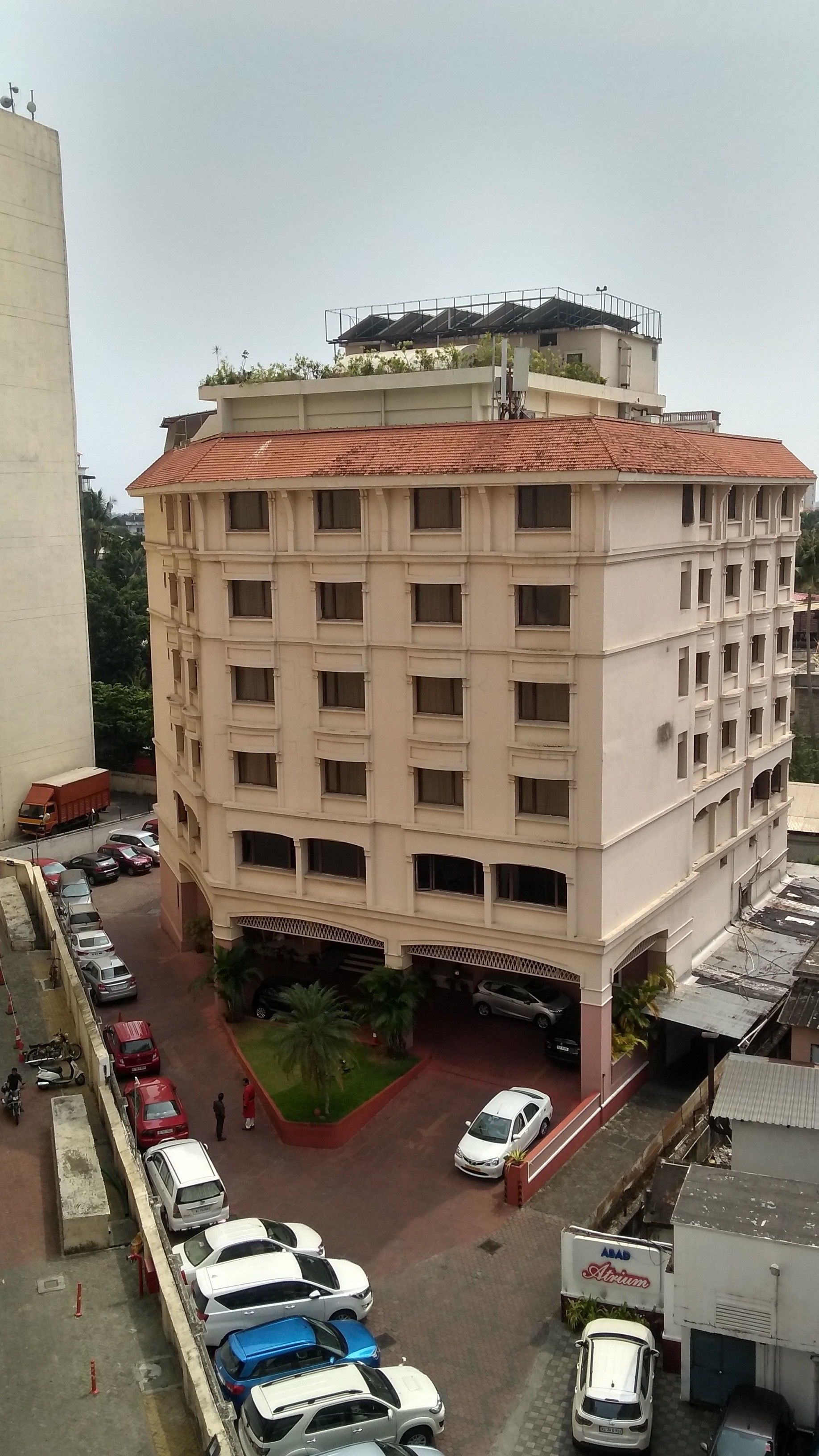 A multi-story building with a flat roof and numerous windows. There is a parking area in front with several cars and a few motorcycles.