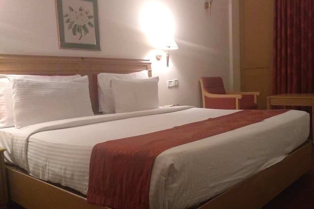 Quarto de hotel com uma cama grande, uma escrivaninha, uma cadeira e um abajur.