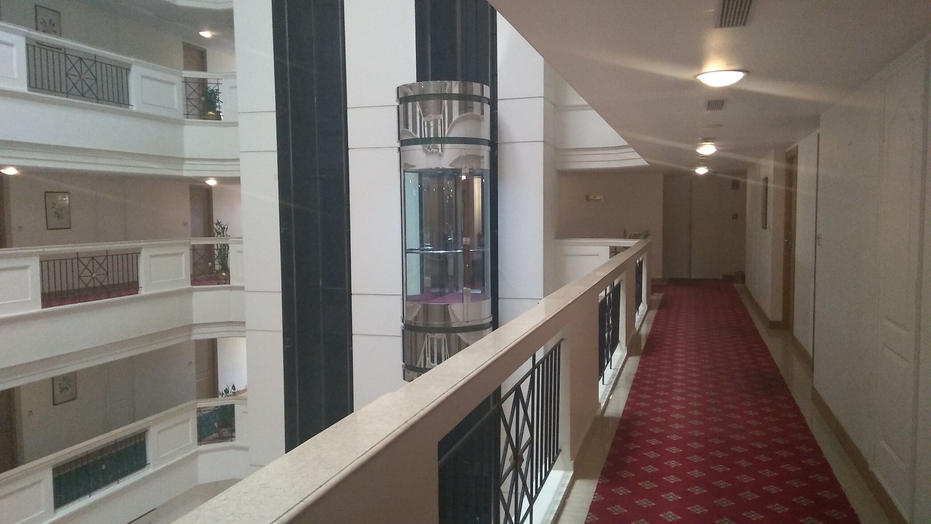 Un pasillo de hotel con alfombra roja, varios pisos y un ascensor central.