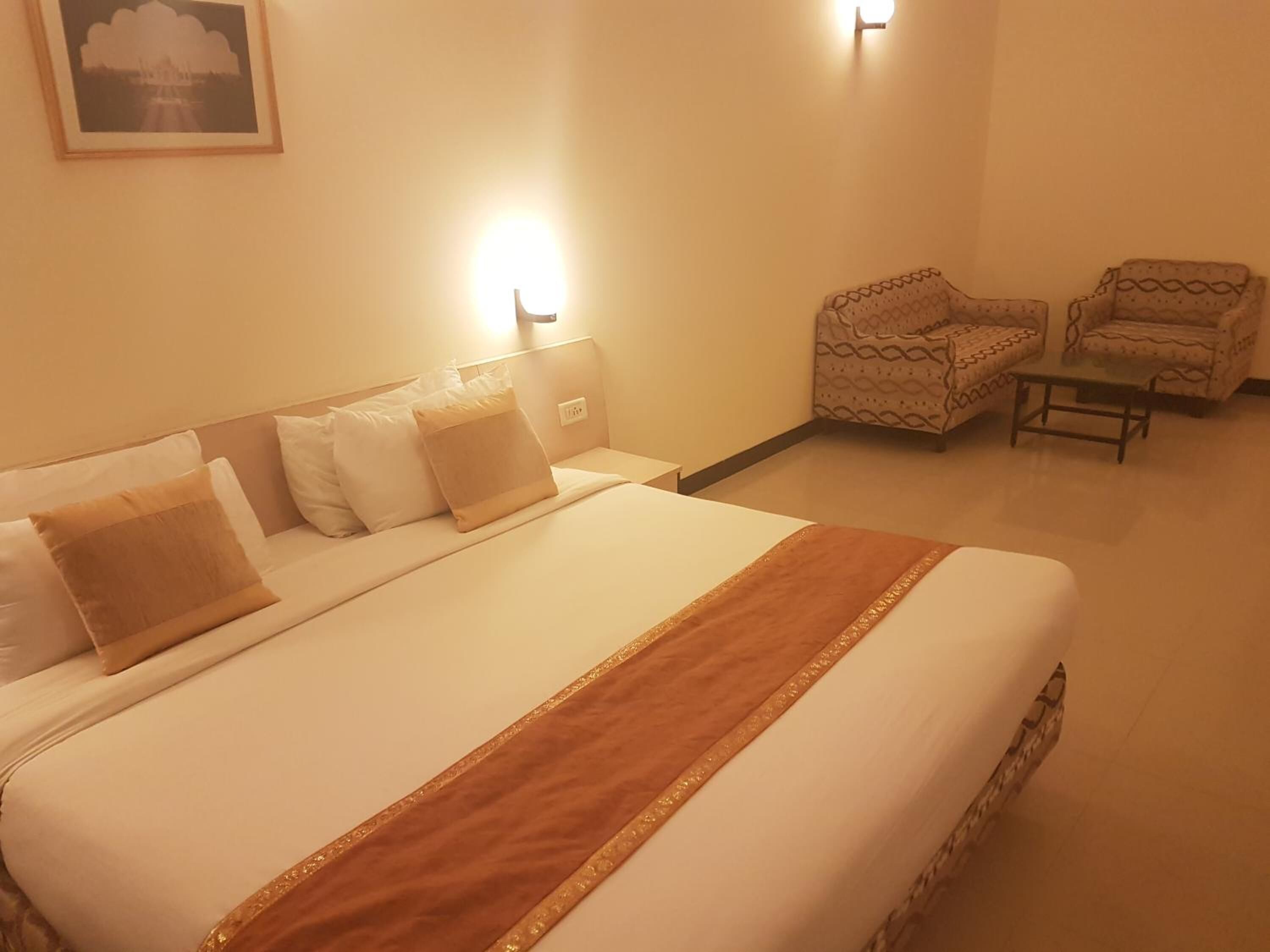 A hotel room with a large bed, two armchairs, a small table, and a wall-mounted light.
