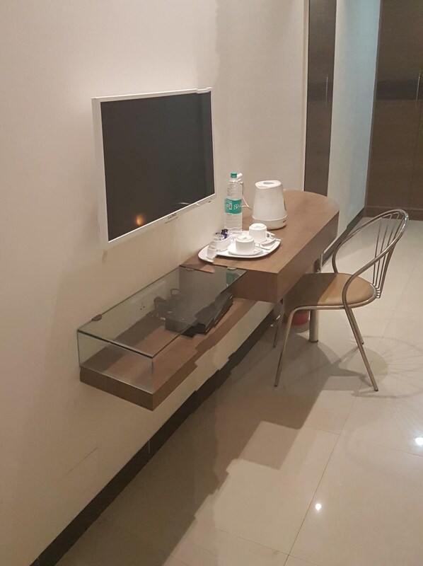 Una habitación de hotel moderna con un escritorio de vidrio, un televisor de pantalla plana montado en la pared, una botella de agua, una taza y una silla.