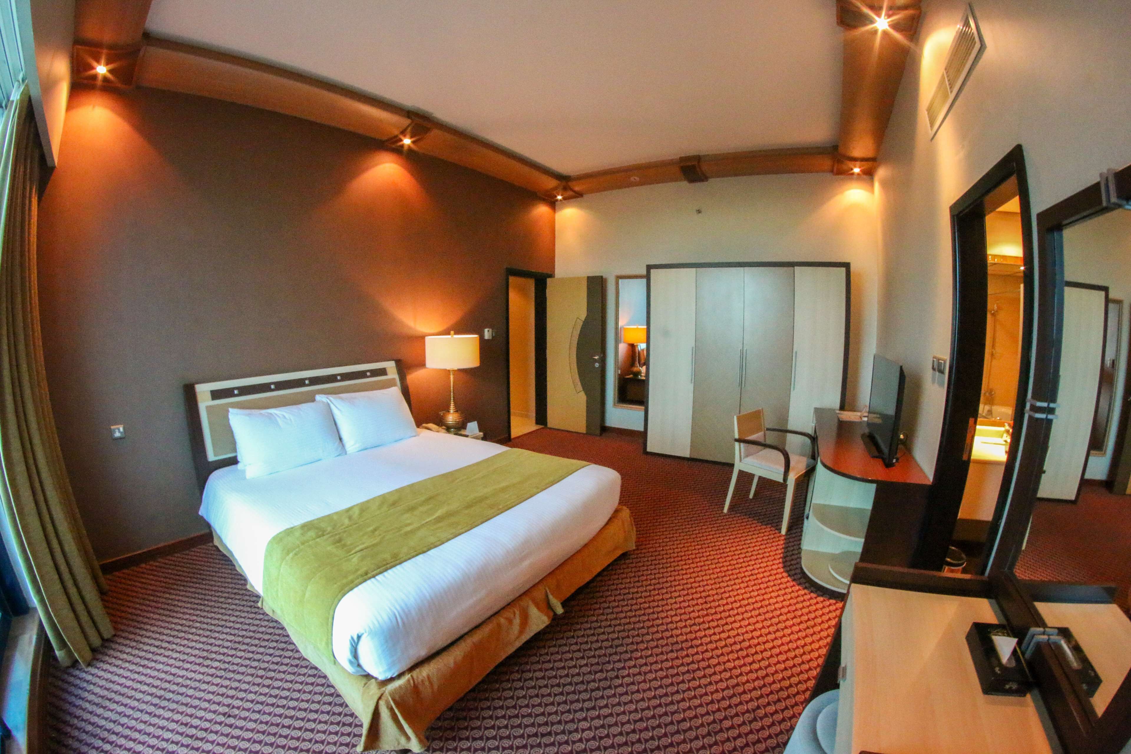 Een hotelkamer met een groot bed, een bureau met stoel, een spiegel en een kledingkast.