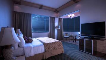 A hotel room with a bed, a television, a desk with a lamp, a chair, and a large window with curtains.