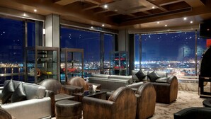 Un salón moderno con sofás y sillones de cuero, amplias ventanas que ofrecen vista a la ciudad de noche.