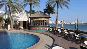 A swimming pool with lounge chairs and a palm tree, overlooking a body of water.