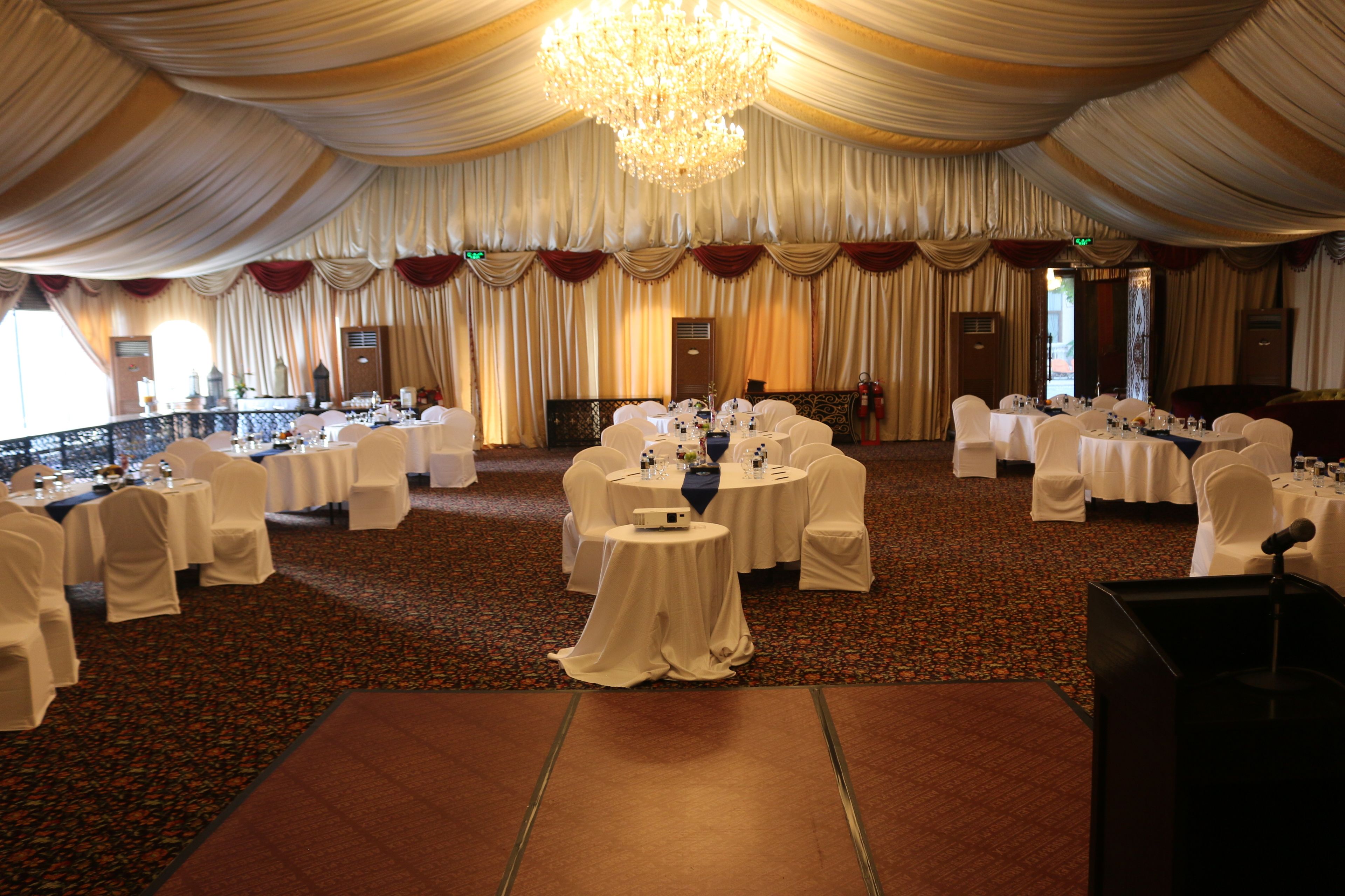 A banquet hall with round tables covered in white tablecloths, white chairs, and a large chandelier.