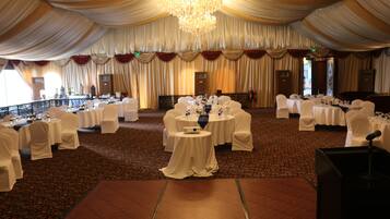 A banquet hall with round tables covered in white tablecloths, white chairs, and a large chandelier.