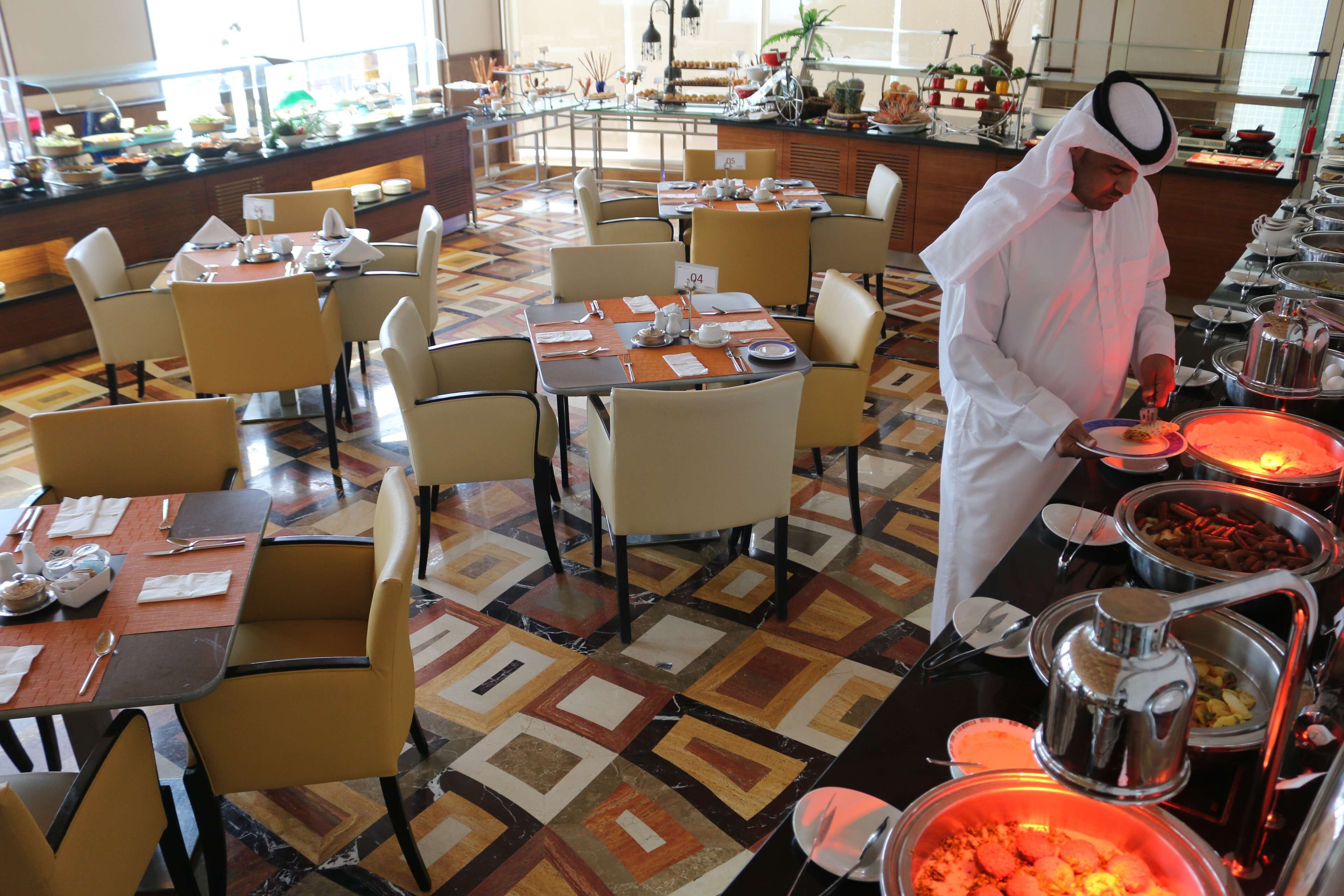 A buffet area with multiple tables and chairs, a variety of food items, and a person serving food.