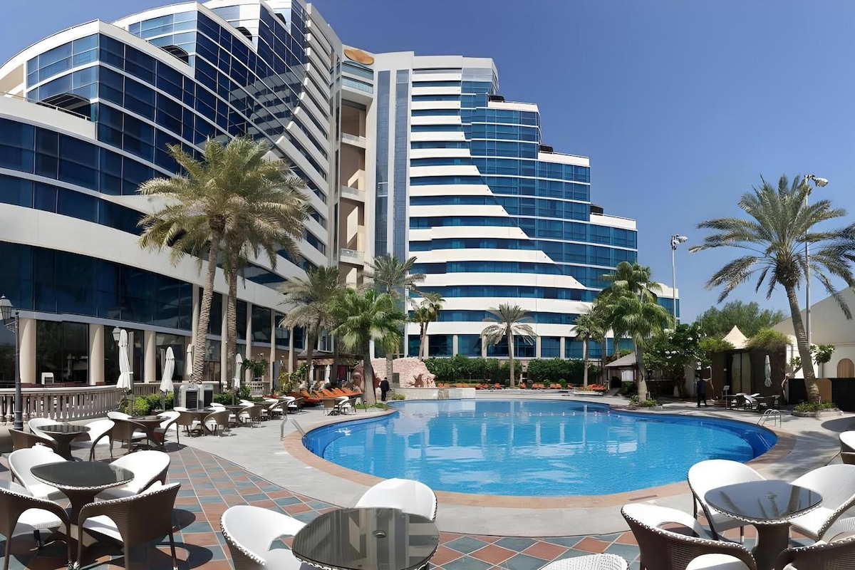 Un hotel con piscina rodeada de sillones de descanso y palmeras.