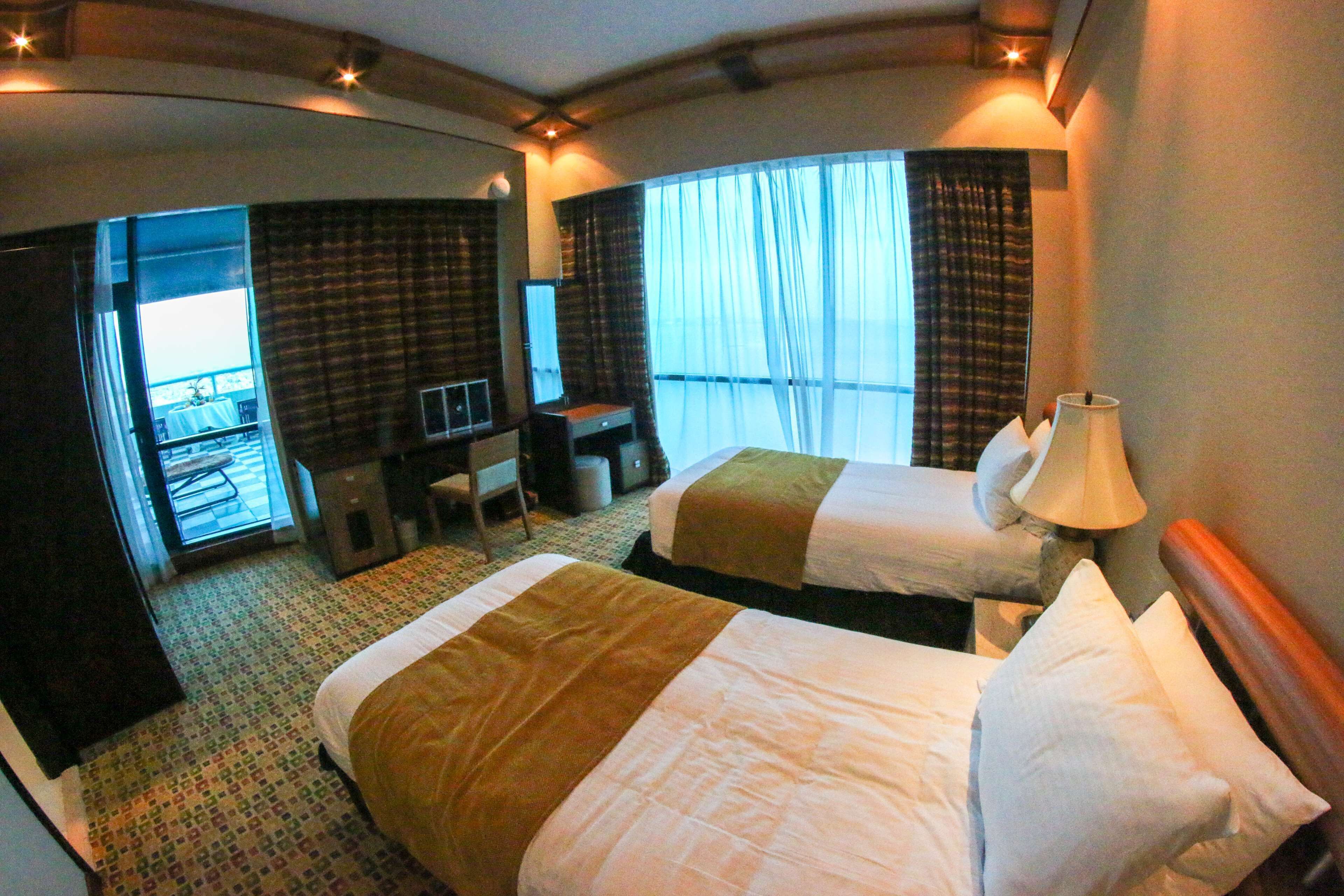 A hotel room with two beds, a desk, a chair, and a view of the balcony.